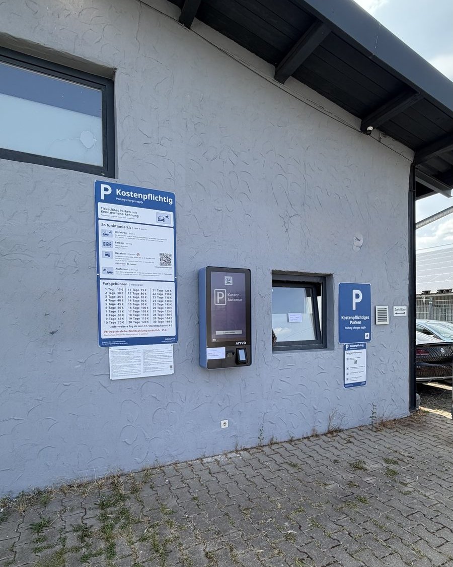 Einfahrt mit Kassenautomat und Beschilderung am Parkplatz Holiday Park, Am Ziegelstadel 4